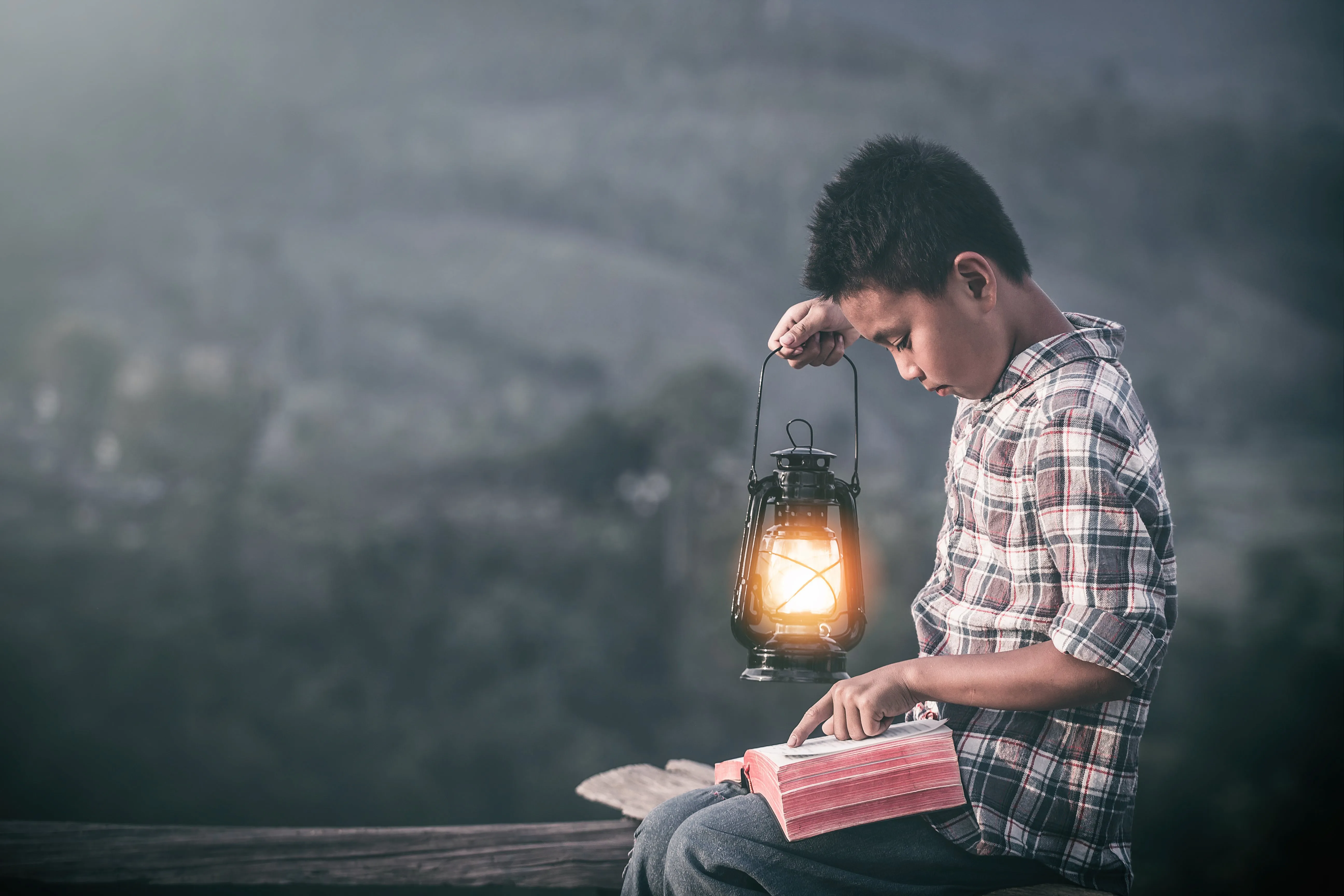 a boy reading the bible with a lattern